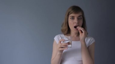 Çekici kadın ilaç, hap ve su içiyor. Gri-mavi arka plan. Sağlık, ilaç, tedavi. 