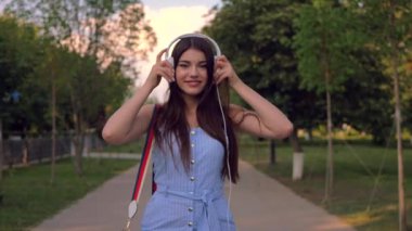 Güzel genç bayan kulaklık takıyor, müzik dinliyor ve elleriyle dans ediyor. Güzel bir kadın zamanını parkta, dışarıda, yazın geçiriyor..