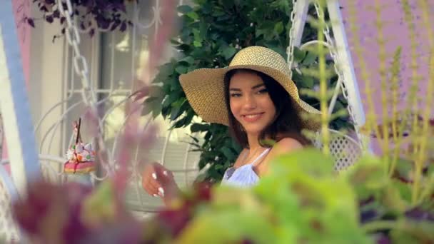 広いつばの帽子の魅力的でエレガントなスペインの女性は カフェのベランダで屋外でサングラスで遊んでいます ピンクの背景 — ストック動画