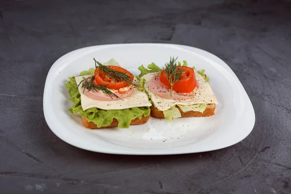 Dos deliciosos sándwiches con hojas de ensalada, tomate y queso en el plato blanco . Imagen De Stock