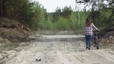 Genç ve çekici bir kadın taşra yolunda bisiklet taşıyor.