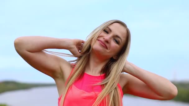 一个有着一头长长的金发的活泼而快乐的女人的画像 这个女孩穿着一件粉红色的T恤 背景是蓝色明亮的天空 — 图库视频影像