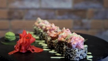 Amerikan dürümleri, karides suşisi ve siyah bir standın etrafında dönme. Japon restoranları için etkileşimli menü. Wasabi ve zencefilli Asya yemeği. Arka planda kırmızı tuğla duvar. 