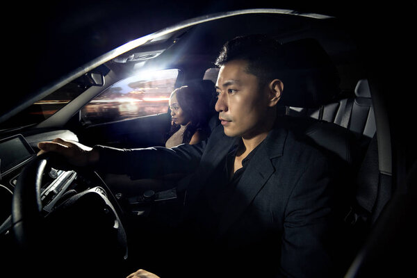 Asian man driving with a black african female date in a car.  They look like they are heading to a nightclub for clubbing nightlife.  The image depicts interracial relationships and lifestyle.