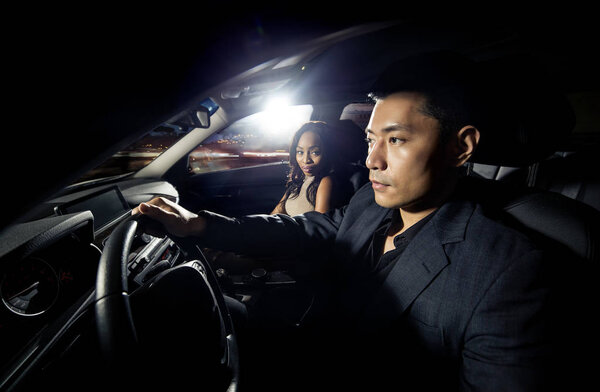 Asian man driving with a black african female date in a car.  They look like they are heading to a nightclub for clubbing nightlife.  The image depicts interracial relationships and lifestyle.