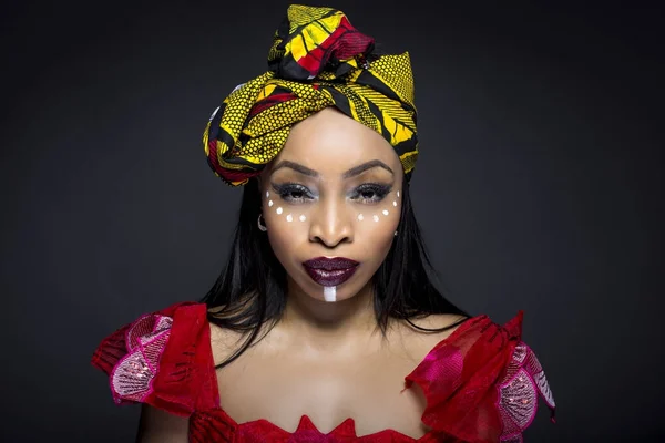 Black female showing African pride by wearing Nigerian traditional clothing and tribal makeup or face painting.  The model is shot in studio in modern vogue fashion style.