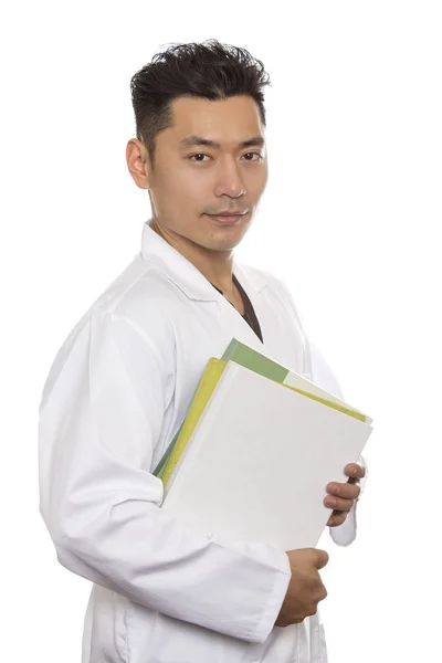 アジア男子医学生は白い背景に分離された白衣を身に着けています 男の人は Heathcare ワーカーまたはインターンです 彼は本を運んでいます — ストック写真