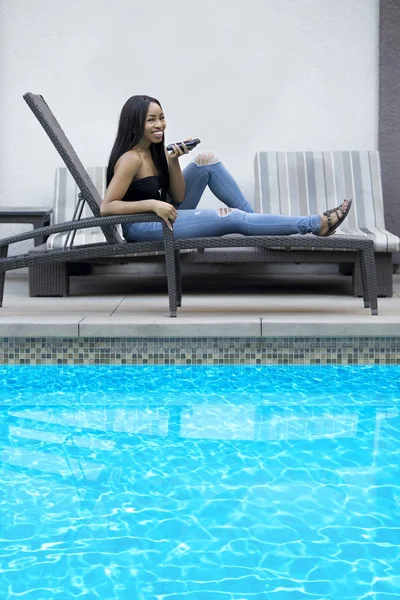 Black female on a speaker phone call in a hotel resort.  She is working while on vacation or dictating reminders on a voice assistant on her cellphone. The woman is sitting on a chair by the hotel pool.