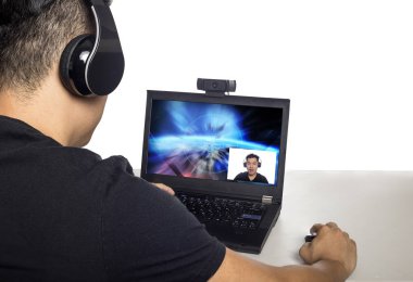 Asian male wearing headphones playing a video game and streaming online with a webcam on a laptop pc.  The image depicts entertainment industry and electronics competition or e-sports.  clipart