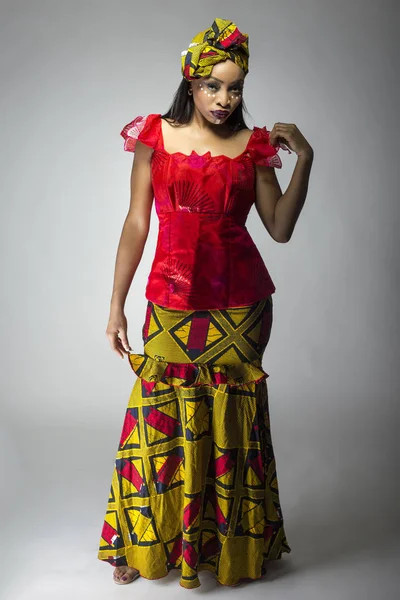 Black female showing african pride by wearing a traditional Nigerian dress and head scarf with tribal face markings or cosmetic makeup.  The costume is red and yellow and shows cultural fashion.