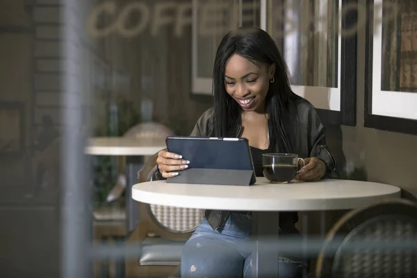 Wifi に接続されたタブレットを使用して黒人女性のウィンドウ表示にあるコーヒー ショップでインターネット 実業家や学生は休憩や仕事やカフェで勉強 — ストック写真