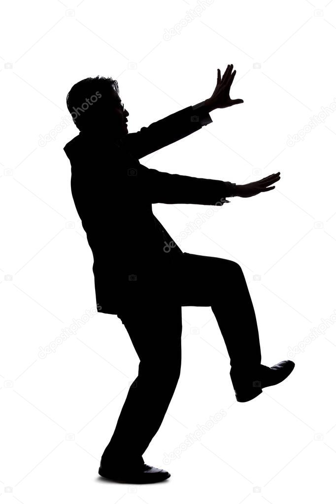 Silhouette of a backlit model posing as a businessman on a white background.  He is balancing or slipping and falling due to an accident