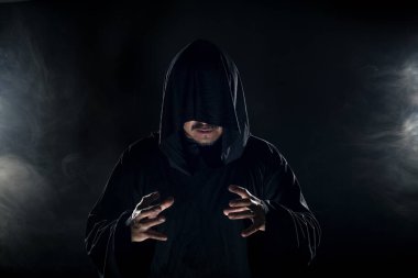 Dumanlı ya da sisli arka planda tarikat lideri gibi görünen koyu renk bornoz giymiş bir adam. Korkunç bir kötü adam gibi görünüyor.