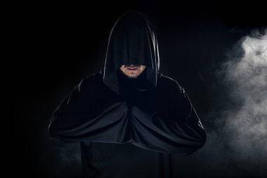 Dumanlı ya da sisli arka planda tarikat lideri gibi görünen koyu renk bornoz giymiş bir adam. Korkunç bir kötü adam gibi görünüyor.
