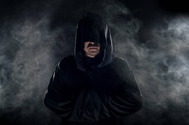 Dumanlı ya da sisli arka planda tarikat lideri gibi görünen koyu renk bornoz giymiş bir adam. Korkunç bir kötü adam gibi görünüyor.