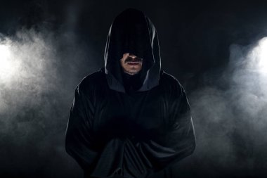 Dumanlı ya da sisli arka planda tarikat lideri gibi görünen koyu renk bornoz giymiş bir adam. Korkunç bir kötü adam gibi görünüyor.