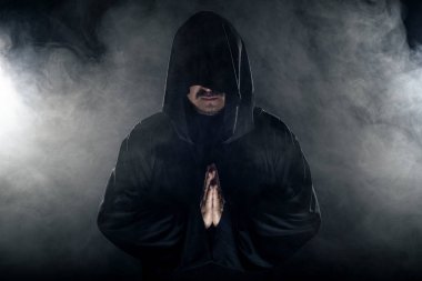 Dumanlı ya da sisli arka planda tarikat lideri gibi görünen koyu renk bornoz giymiş bir adam. Korkunç bir kötü adam gibi görünüyor.