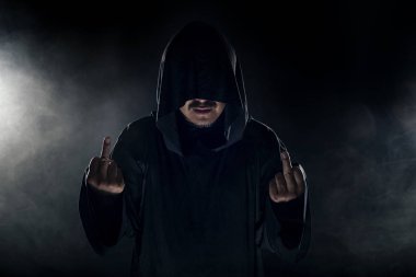 Dumanlı ya da sisli arka planda tarikat lideri gibi görünen koyu renk bornoz giymiş bir adam. Korkunç bir kötü adam gibi görünüyor.