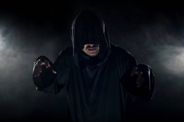 Dumanlı ya da sisli arka planda tarikat lideri gibi görünen koyu renk bornoz giymiş bir adam. Korkunç bir kötü adam gibi görünüyor.