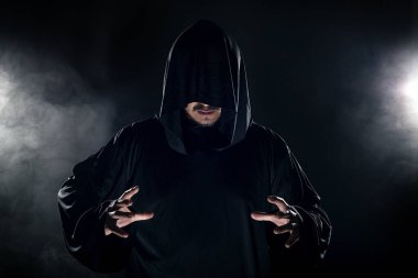 Dumanlı ya da sisli arka planda tarikat lideri gibi görünen koyu renk bornoz giymiş bir adam. Korkunç bir kötü adam gibi görünüyor.