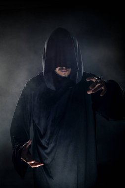Dumanlı ya da sisli arka planda tarikat lideri gibi görünen koyu renk bornoz giymiş bir adam. Korkunç bir kötü adam gibi görünüyor.
