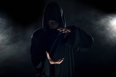 Dumanlı ya da sisli arka planda tarikat lideri gibi görünen koyu renk bornoz giymiş bir adam. Korkunç bir kötü adam gibi görünüyor.