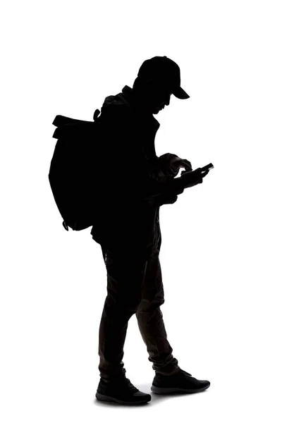 旅行者やハイカーのトレッキングのように見えるバックパックを着て男のシルエット 携帯電話を使ってる — ストック写真