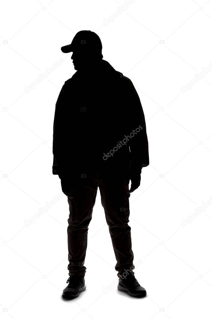 Silhouette of a man wearing a backpack looking like a traveler or hiker trekking.  He is patiently standing and waiting 