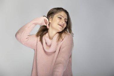 Gri arka planda pembe bir kazak giyen beyaz bir kadının portresi. Mutlu ve neşeli görünüyor.