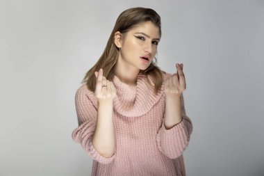 Gri arka planda pembe bir kazak giyen beyaz bir kadının portresi. İfadesi bir para hareketi.