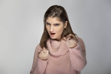 Gri arka planda pembe bir kazak giyen beyaz bir kadının portresi. İzleyiciyi işaret ediyor.