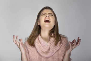 Gri arka planda pembe bir kazak giyen beyaz bir kadının portresi. Kızgın ve stresli görünüyor.