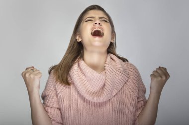 Gri arka planda pembe bir kazak giyen beyaz bir kadının portresi. Kızgın ve stresli görünüyor.