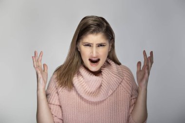 Gri arka planda pembe bir kazak giyen beyaz bir kadının portresi. Kızgın ve stresli görünüyor.