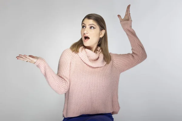 灰色の背景にピンクのセーターを着た若い白人女性の肖像画を閉じます 彼女は広告のようなものを提示している — ストック写真