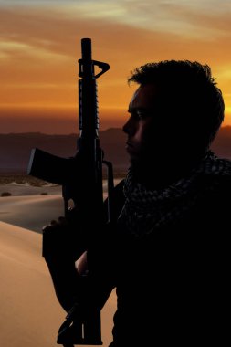 Çölün gölgesinde elinde tüfekle dinlenen bir erkek askerin silueti. Özel askeri, milis ya da özel kuvvetleri gösteriyor. Yorgun ve evini özlemiş görünüyor.