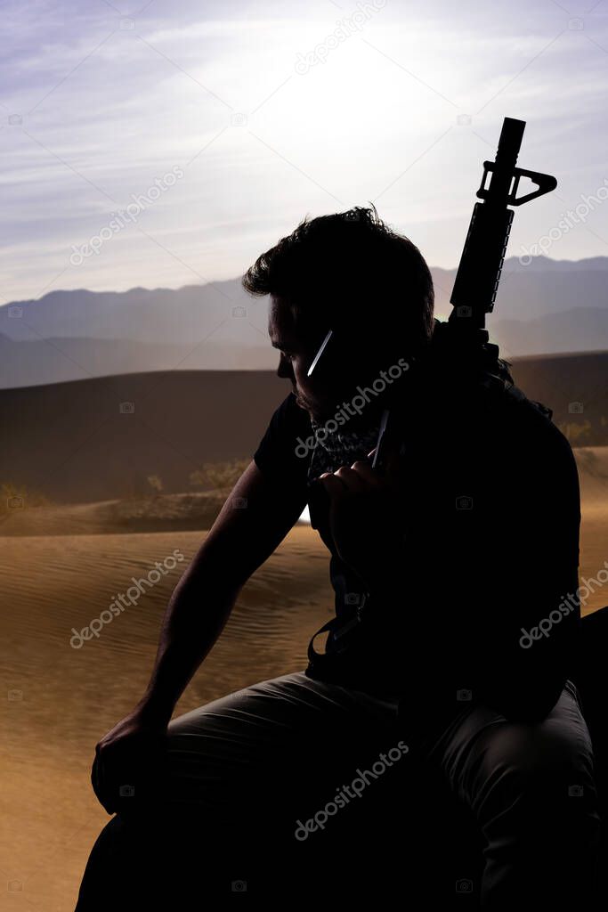 Silhouette of a male soldier resting in the shade on a desert and holding a rifle.  Depicts the private military industry, militia, or special forces.  He looks tired and homesick