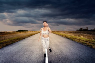 Spor kıyafetleri giyen, koşan ya da izole bir yolda tek başına koşan sağlıklı bir kadın. Sosyal uzaklık sırasında egzersiz yapmak için. Sağlıklı bir yaşam tarzı sürdürmeye kararlı.