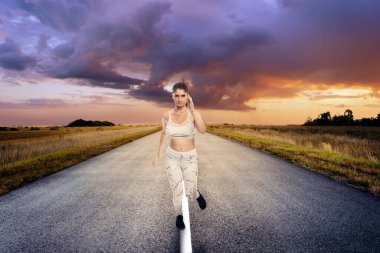 Spor kıyafetleri giyen, koşan ya da izole bir yolda tek başına koşan sağlıklı bir kadın. Sosyal uzaklık sırasında egzersiz yapmak için. Sağlıklı bir yaşam tarzı sürdürmeye kararlı.