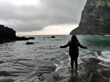 Kolları açık bir kadın Güney Kore 'deki Jeju Adası' nda dağları, bulutları ve yağmuru ıslatıyor.
