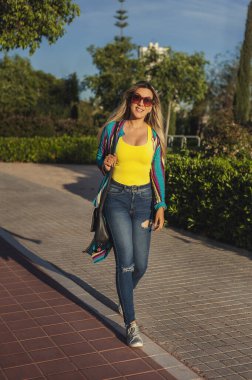 Parkta güneş gözlükleriyle yürüyen mutlu yetişkin kadın.