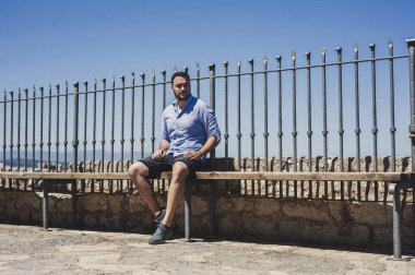 Genç adam çitte oturuyor.