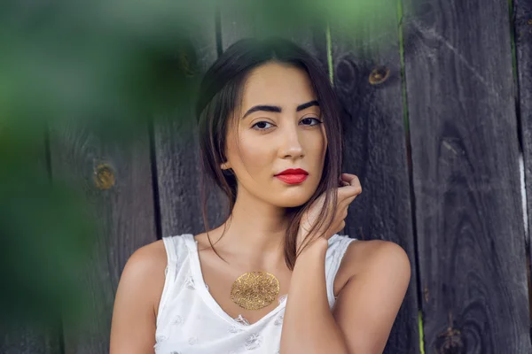 Chica morena en un parque en el verano descansando blusa blanca en el fondo de la cerca de madera, estilo de vida de moda, mirada suave. Maquillaje sensual, piel bronceada y lápiz labial rojo brillante . — Foto de Stock