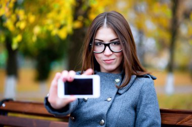 Gözlüklü, Bahar, sonbahar parkta açık havada güzel genç kadın hava ceket, telefon gösterir elini, kentsel yaşam, metin, smartphone reklam, fikir kavramı 