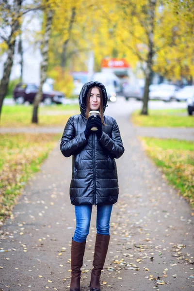 Mädchen in Jacke mit Kapuze, hält einen Kaffee oder Tee, junge genießt die Natur und Sport, Frühling Herbst, Lifestyle, schwarz, das Konzept des Frühstücks, Handschuhe — Stockfoto