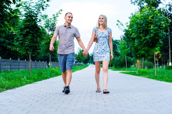 El tipo con chica en un parque de verano cogido de la mano caminando relajarse, disfrutar de paseo, feliz concepto familiar lema de su texto en segundo plano. Vida en la ciudad. gran cantidad de verduras . — Foto de Stock