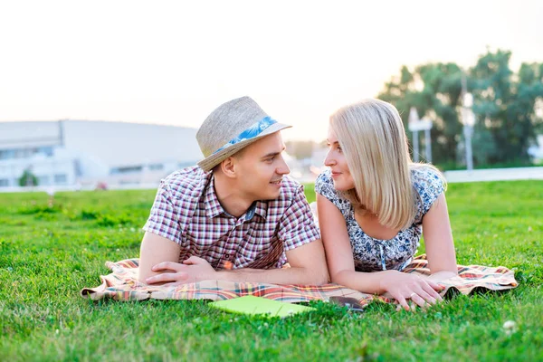 Jeune couple assis sur l'herbe dans le parc, concept d'événement d'une famille, relation amusante. Mode de vie dans l'amour heureux. En plein air jour d'été. Ils se sourient et se regardent . — Photo