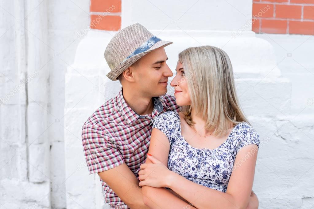 Young couple, looking at each other a bright sunny day in city of great outdoors, happy family concept, idea good relationship. Smile and smotryad  . Against background   white brick wall.