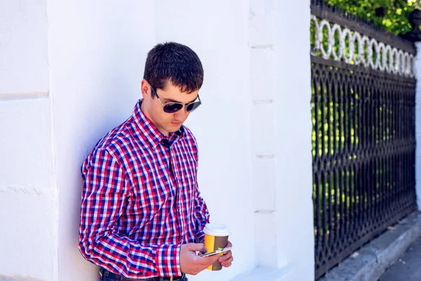 Mann an Wand, mit Kaffee und Telefon, im Sommer mit Brille und Hemd, SMS lesen auf dem Smartphone, Geschäftsmann. — Stockfoto