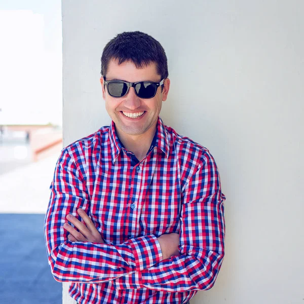 Um homem está na cidade de uma parede branca, camisa de verão, descansando, schaslivo empresário sorrindo ao ar livre. O conceito de emoção, óculos escuros. Estilo de vida jovem . — Fotografia de Stock